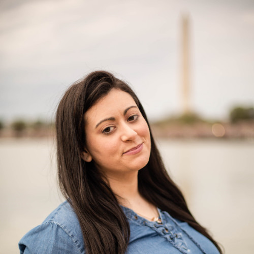 Photo of Jennifer Heiser with the Washington Monument blurry in the background. Jennifer is wearing a jean top with her hair down.